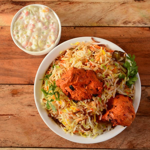 Chicken Biryani with raita, a flavorful Indian rice dish with marinated chicken and spices.